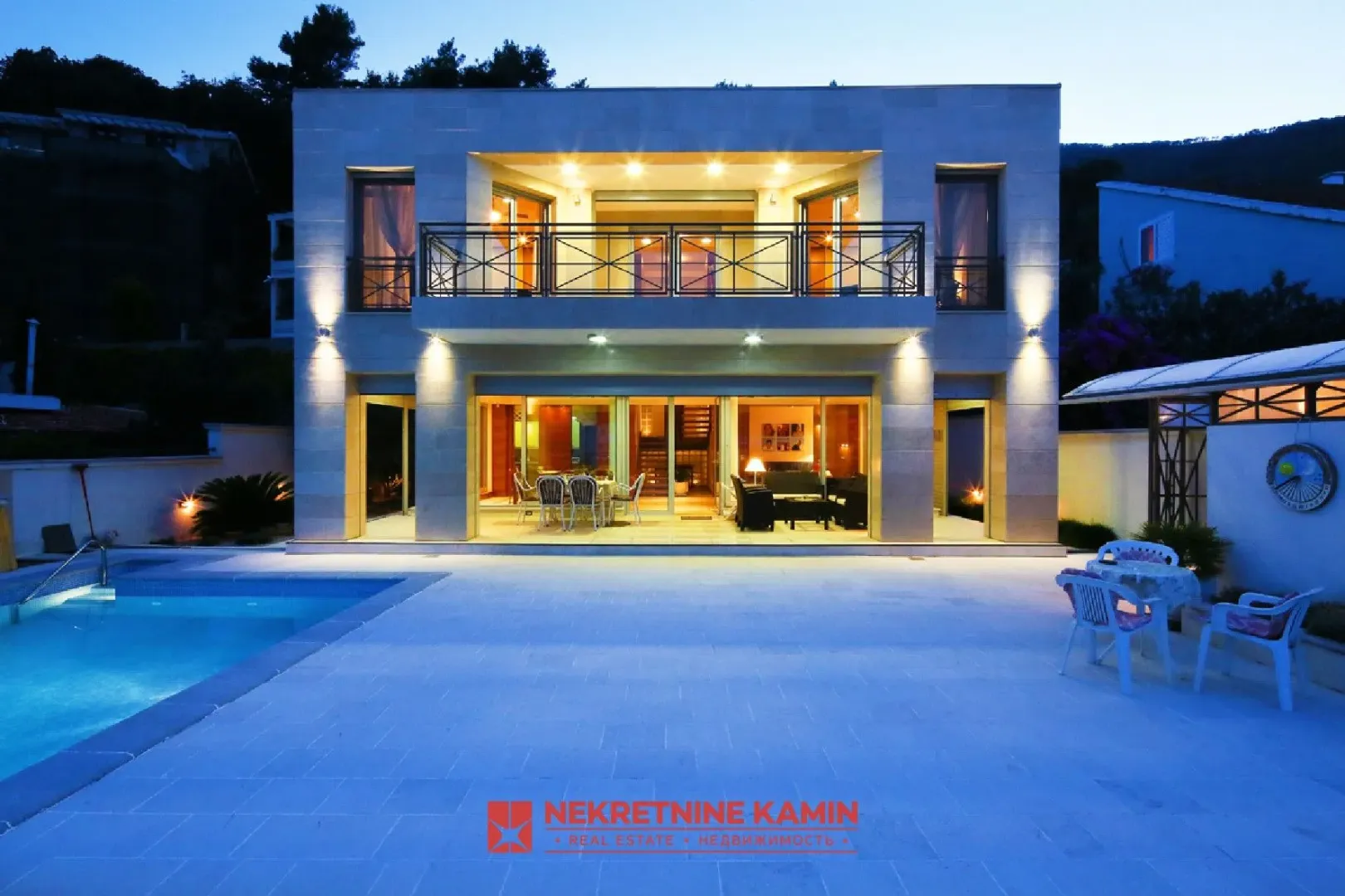 View of the illuminated facade of a luxury house with a swimming pool in the evening.