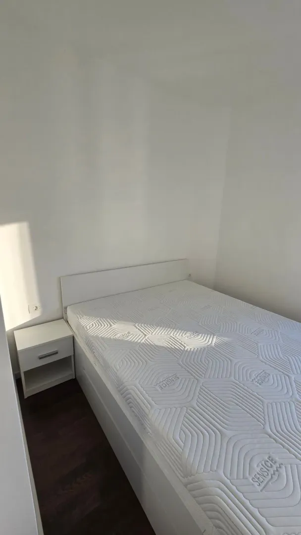 Svjetla spavaća soba sa bijelim krevetom i noćnim stočićem.