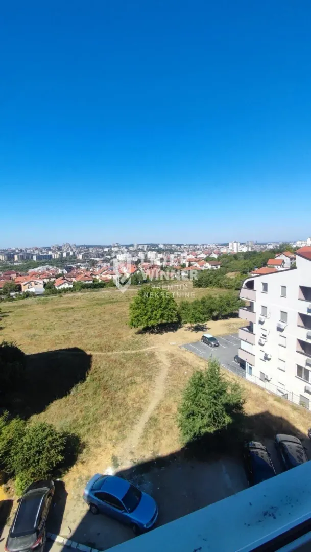 Pogled iz visine na gradski pejzaž i okolne objekte sa parkingom.