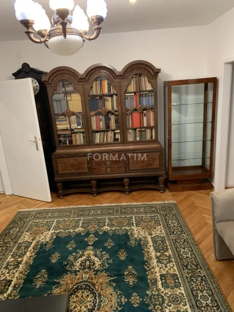 Dnevna soba sa klasičnom drvenom bibliotekom i velikim tepihom na podu.