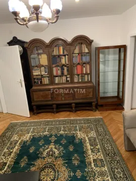 Dnevna soba sa klasičnom drvenom bibliotekom i velikim tepihom na podu. - image 6