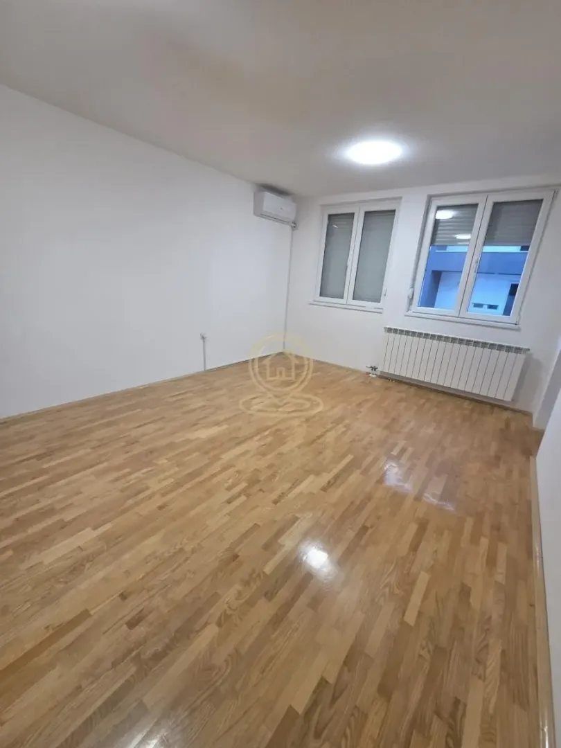 Prazna soba sa parketom i belim zidovima.