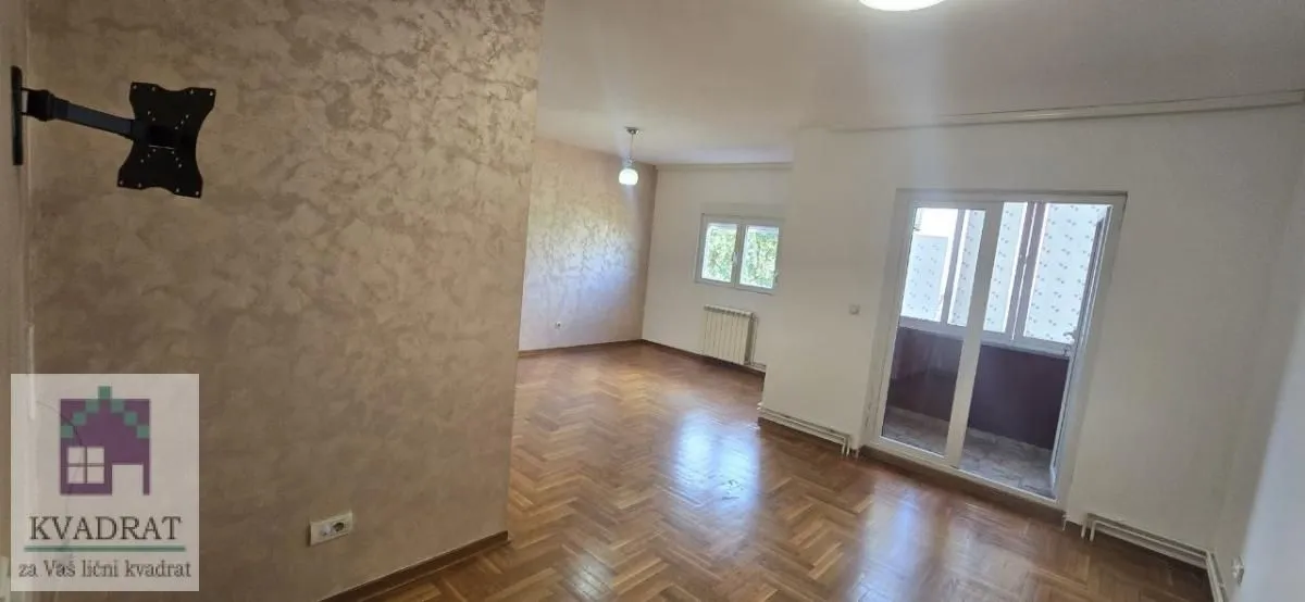 Prostrana prazna dnevna soba sa parketom i izlazom na terasu.