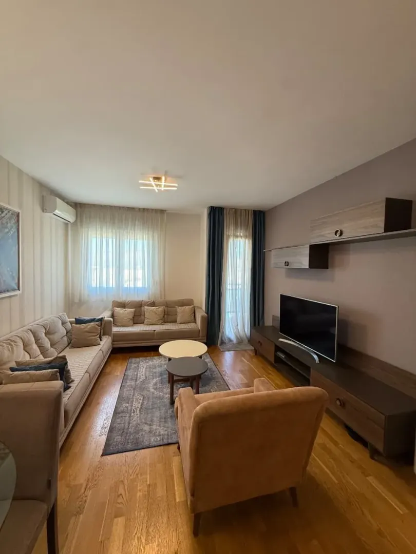 Dnevna soba sa garniturom, foteljom, televizorom i drvenim namještajem.