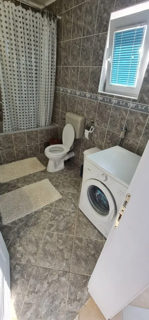 Kupatilo sa pločicama, kadom, WC šoljom i veš mašinom.