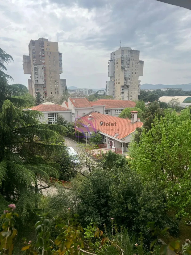 Pogled sa prozora na okolne zgrade i zelene površine.