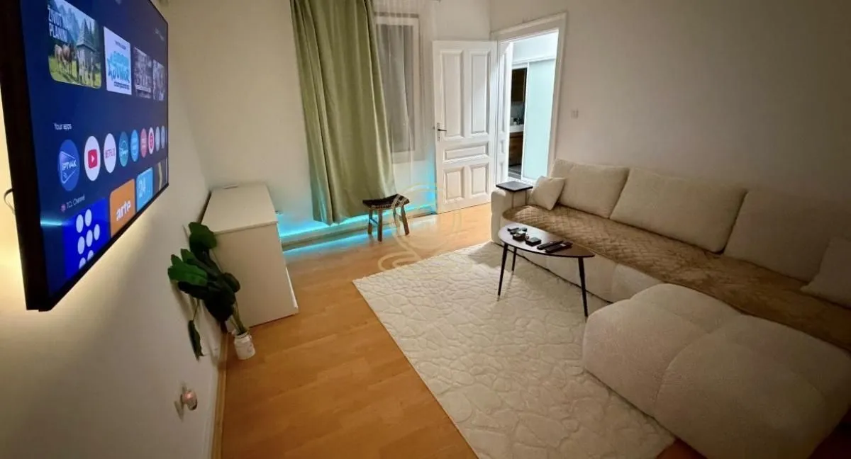 Dnevna soba sa ugaonom garniturom, televizorom i tepihom.