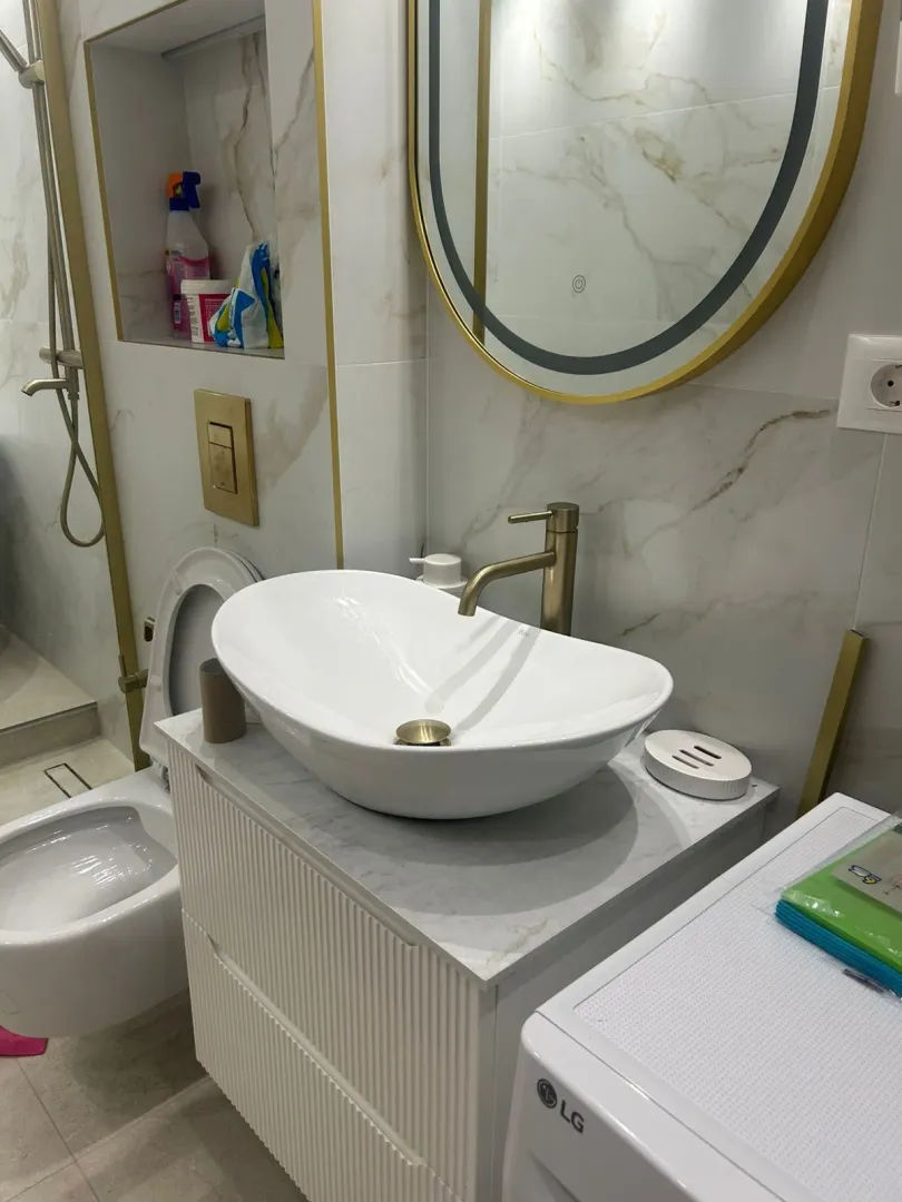 Moderne kupatilo sa umivaonikom, zlatnim slavinama i WC šoljom.