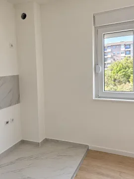 Prazna prostorija sa svijetlim zidovima, prozorom i kombinacijom keramičkih pločica i laminata na podu. - image 3