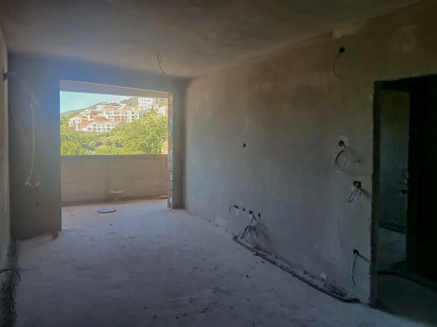 Nezavršena prostorija u sivoj fazi sa pogledom na naselje kroz otvor.