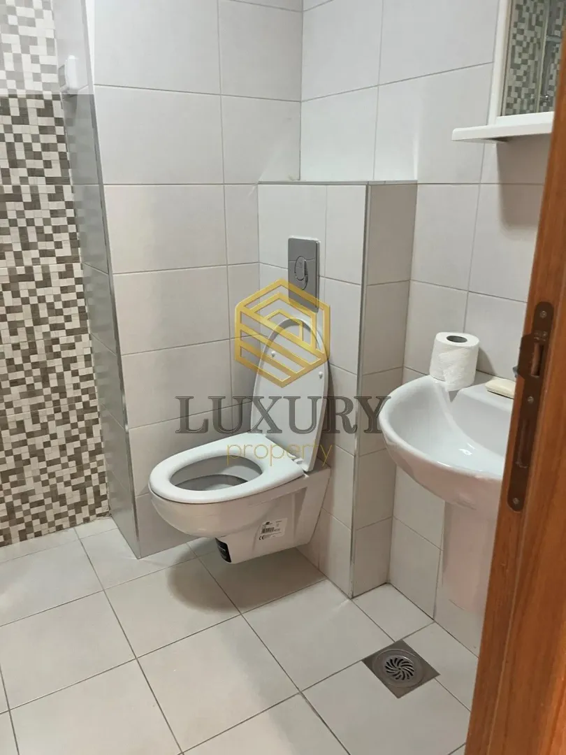 Small bathroom with white tiles, toilet bowl, and sink.