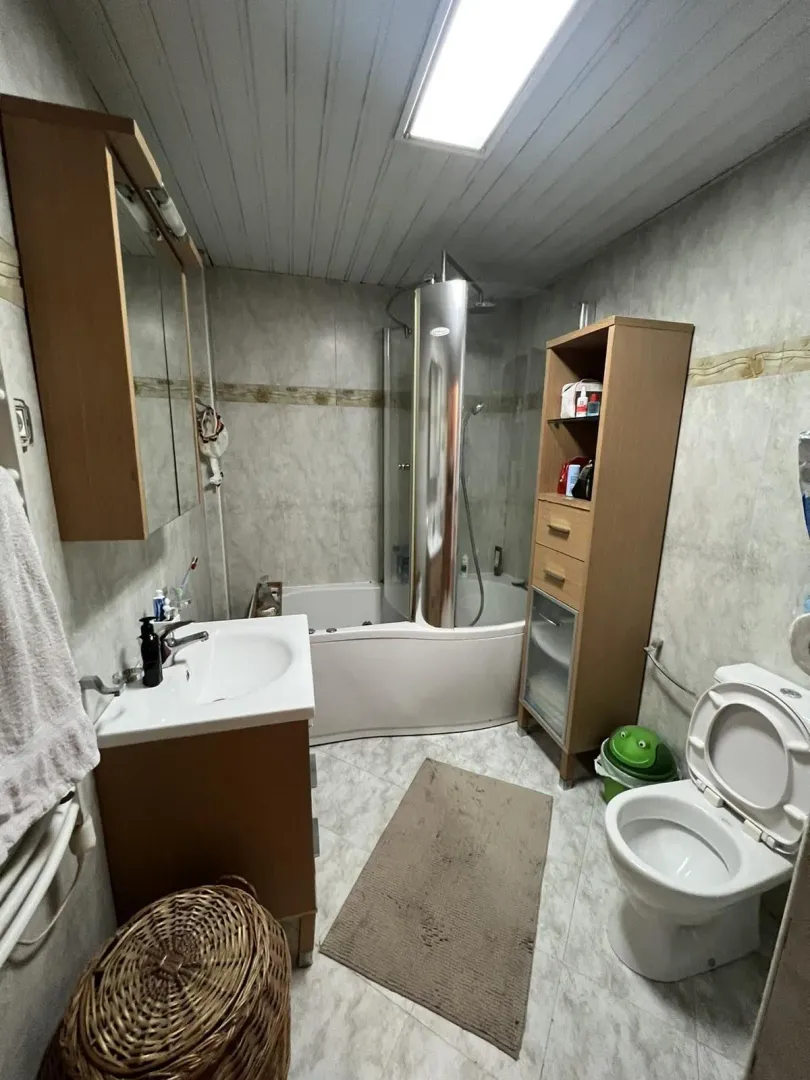 Funkcionalno kupatilo sa kadom, lavaboom i drvenim ormarićima.