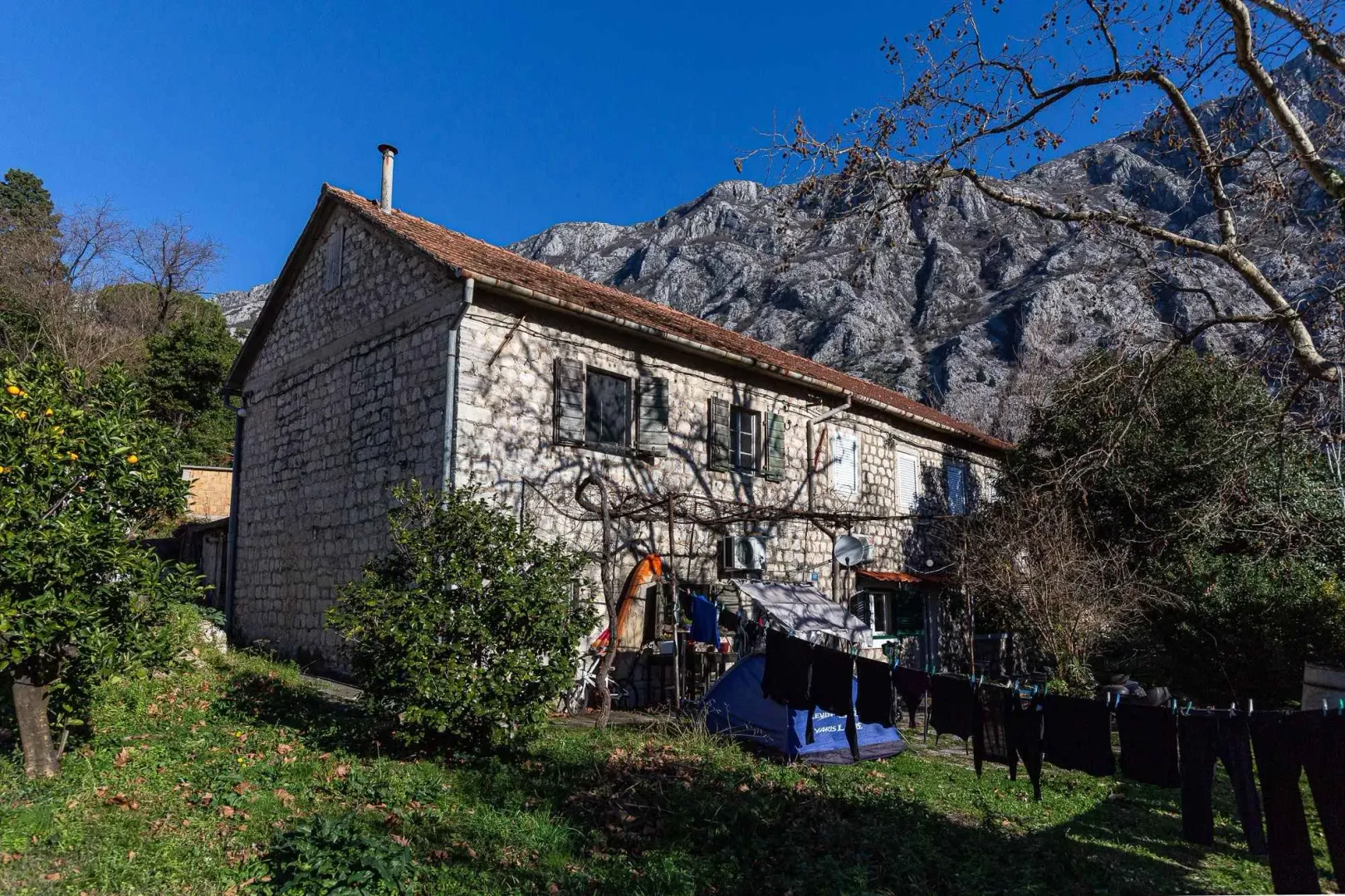 Pogled na spoljašnjost tradicionalne kamene kuće sa dvorištem u podnožju planine.