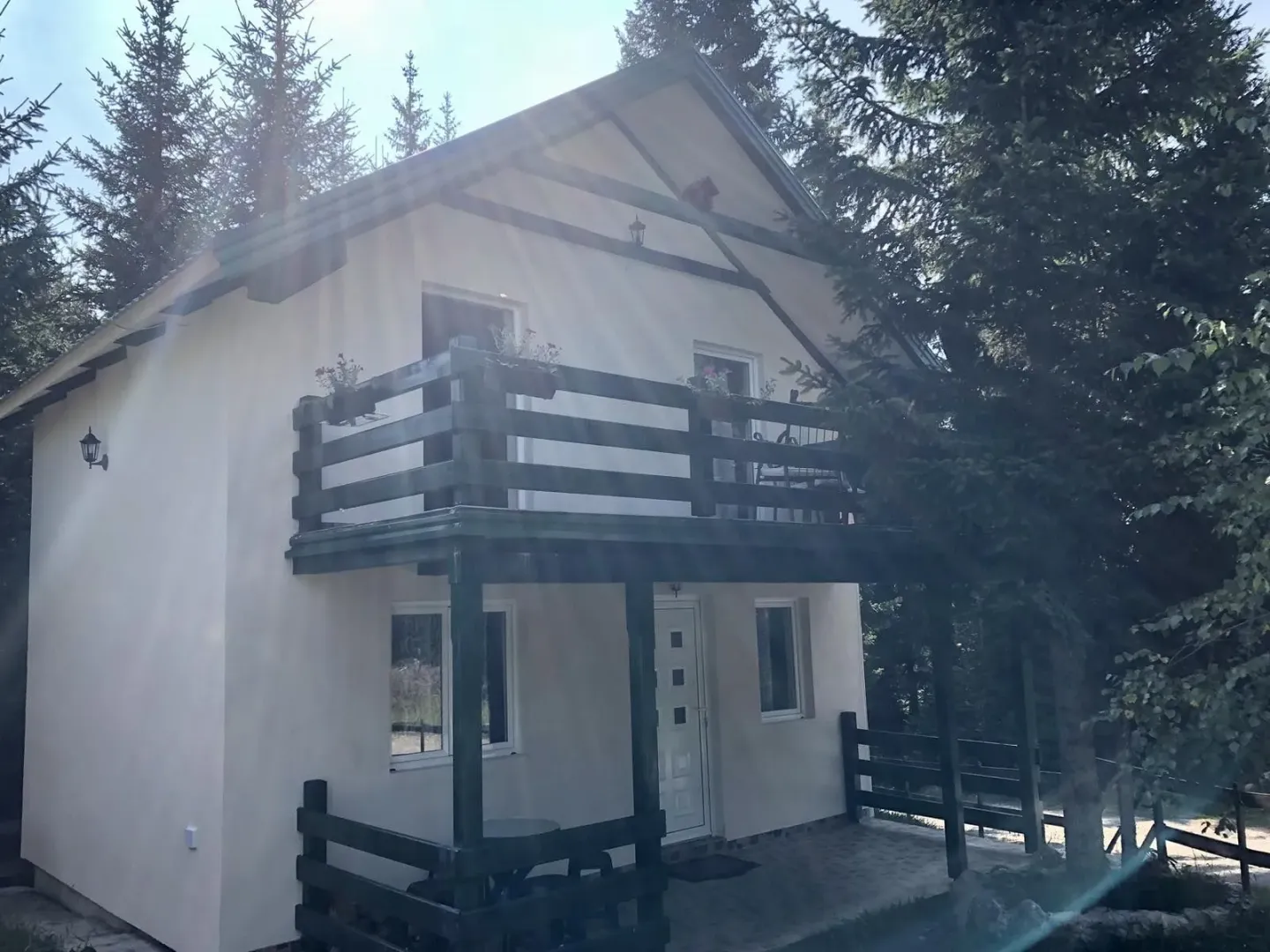 Dvospratna planinska kuća sa balkonom okružena drvećem.