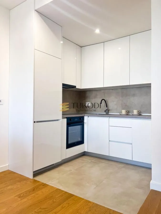 Modern white kitchen with built-in appliances and ceramic tile flooring.