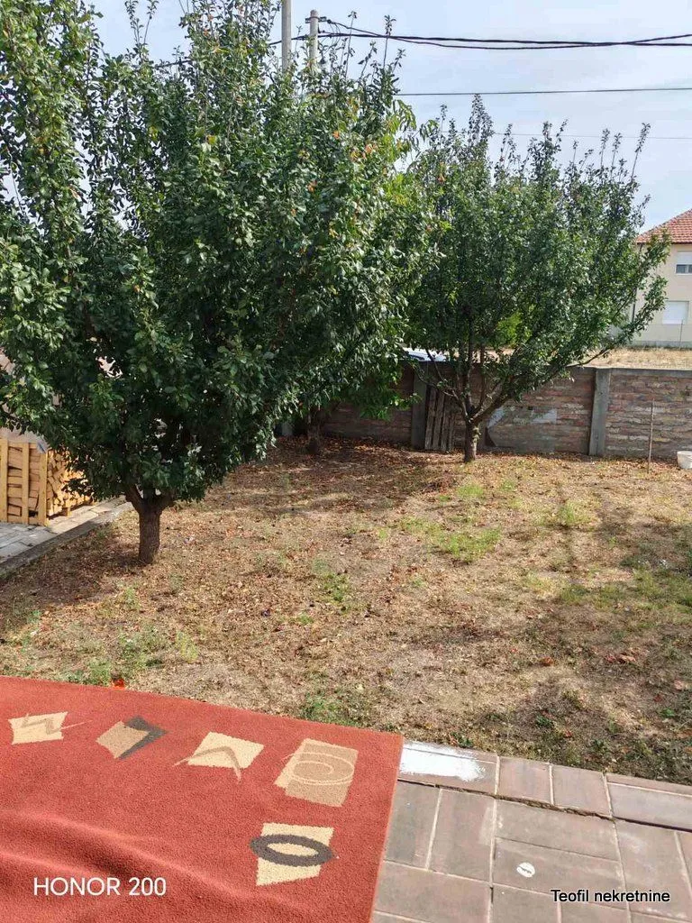 Pogled na uređeno dvorište sa drvećem i ogradom.