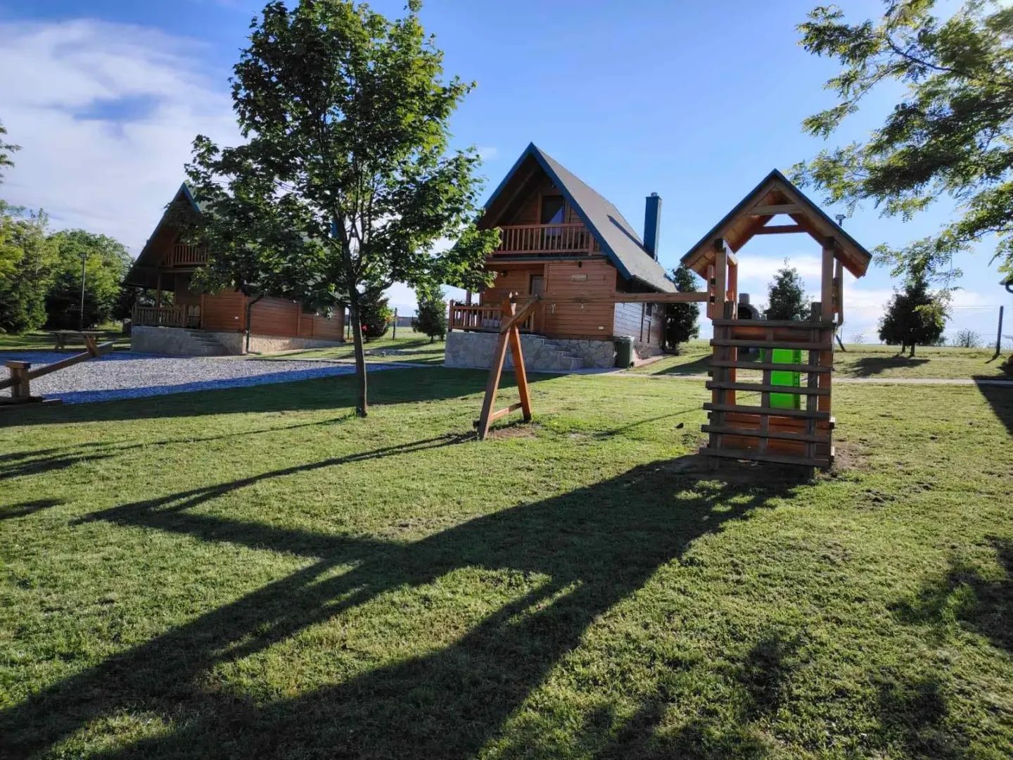 Pogled na drvene vikendice i uređeno dvorište sa dečijim igralištem.