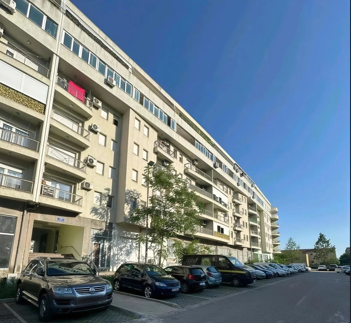 Spoljašnji izgled stambene zgrade sa parkingom i prilazom.