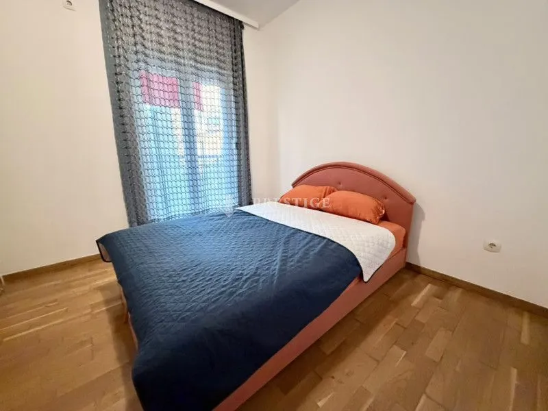 Spavaća soba sa bračnim krevetom, drvenim podom i prozorom sa zavjesom.