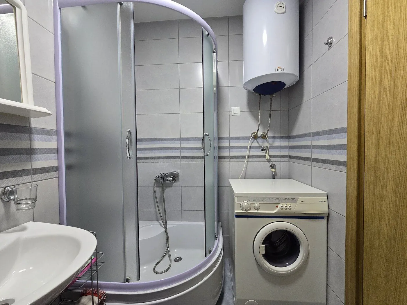 Manje kupatilo sa tuš kabinom, umivaonikom, bojlerom i veš mašinom.