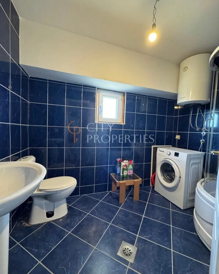 Bathroom tiled in blue with a toilet, sink, shower cabin, and washing machine.