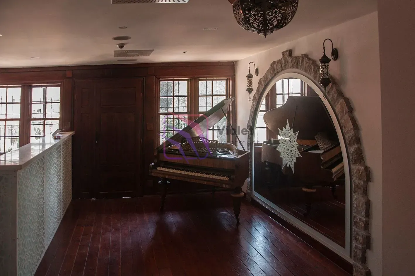 Spacious living room with wooden flooring, a piano, and a large mirror in a stone frame.