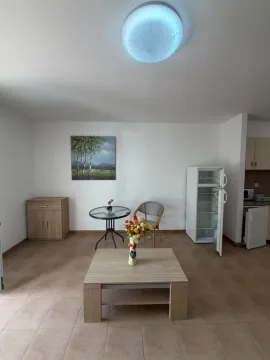 Dnevni boravak sa stolom, stolicom i manjim frižiderom u uglu. - image 4