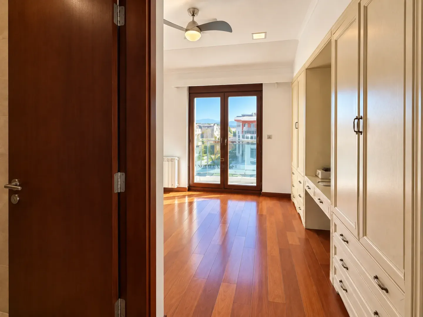 View from the hallway into the bedroom with built-in wardrobes and balcony doors.