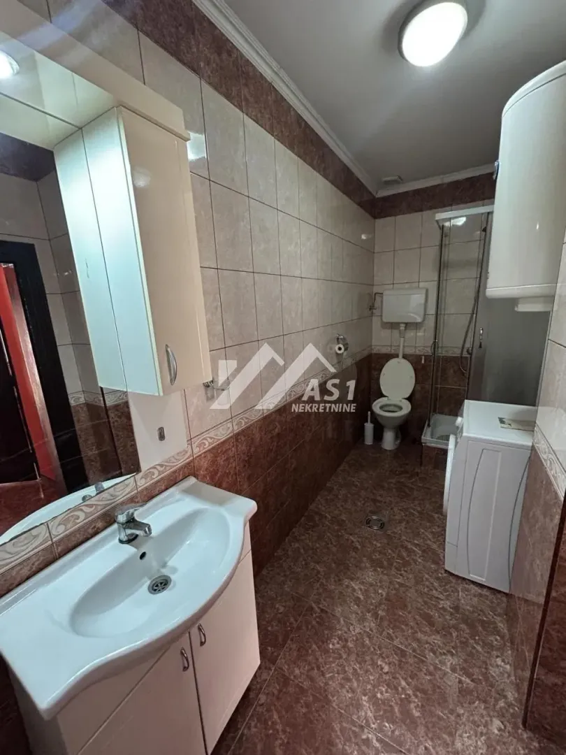 Kupatilo opremljeno umivaonikom, WC šoljom, tuš kabinom i veš mašinom.