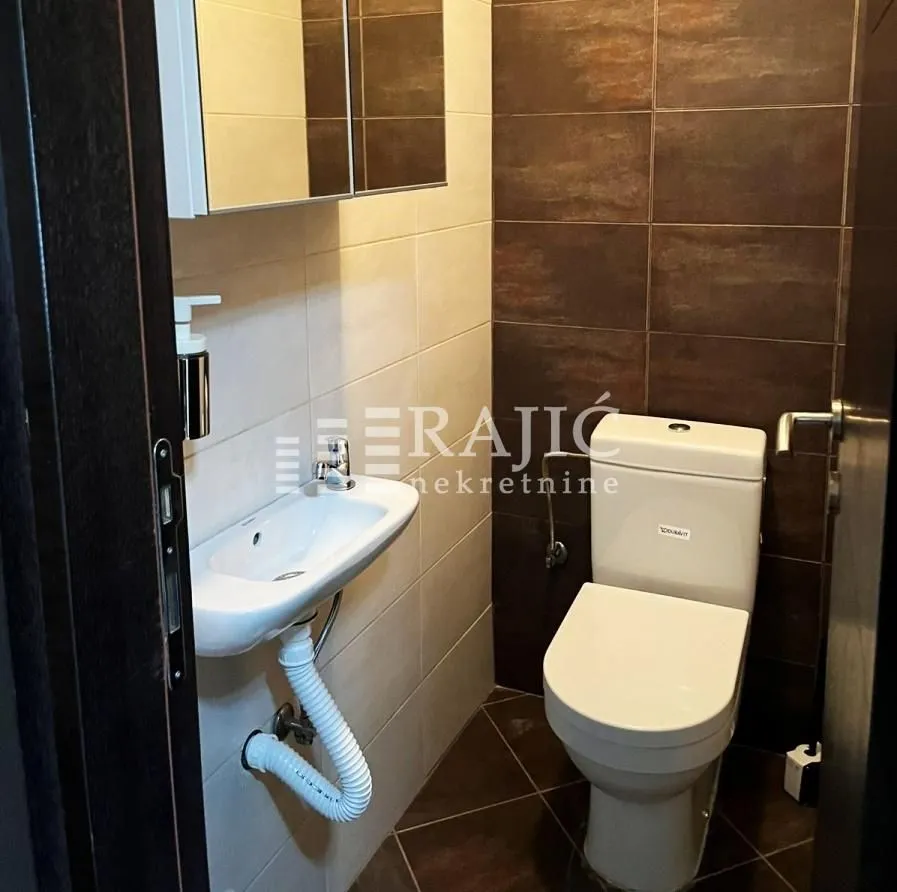 Small bathroom with a sink and toilet, tiled with ceramic tiles.