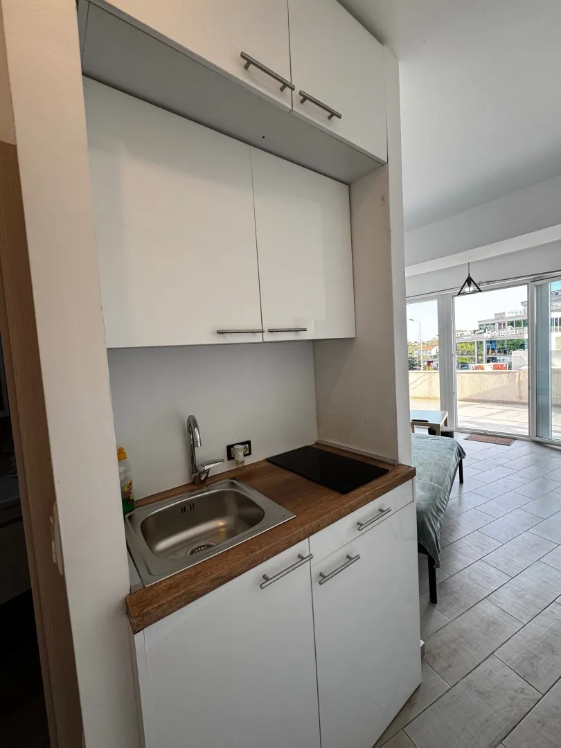 Small white kitchen with a sink and built-in hob, connected to the room and terrace.