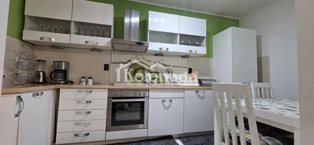 Kuhinja opremljena belim elementima i ugradnim aparatima sa trpezarijskim stolom.
