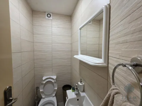 Small bathroom lined with beige tiles featuring a toilet, washbasin, and mirror. - image 7