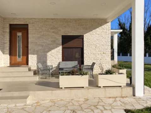 Covered terrace in front of the house entrance with seating furniture and planters. - image 3