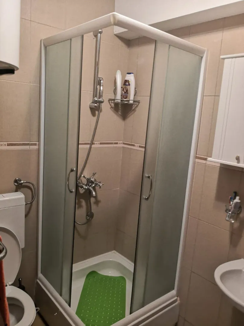 Kupatilo opremljeno tuš kabinom, umivaonikom i wc šoljom u bež tonovima.