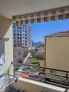View of surrounding buildings and the sea from a balcony with an awning and a drying rack. - image 2