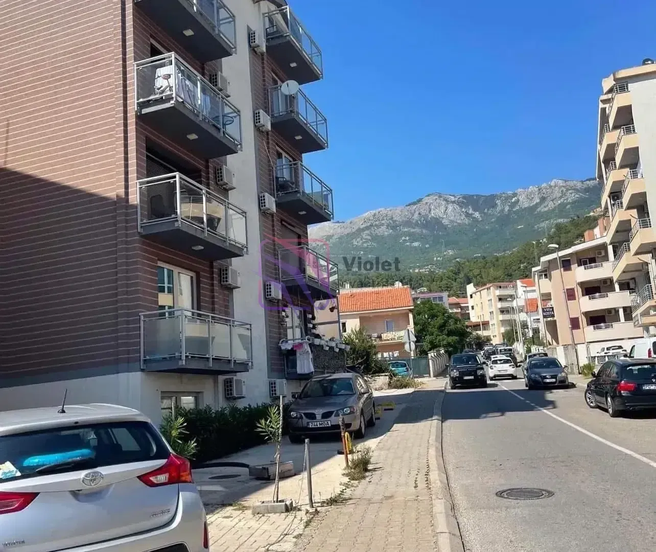 Pogled na ulicu i spoljašnjost zgrade sa balkonima.