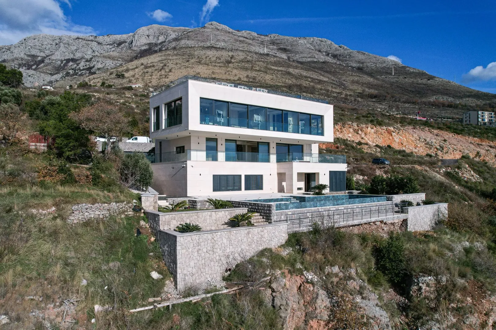 Pogled na modernu višespratnu kuću sa bazenom i planinskim pejzažom u pozadini.