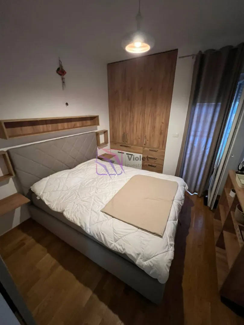 Namještena spavaća soba sa bračnim krevetom, plakarom i drvenim podom.