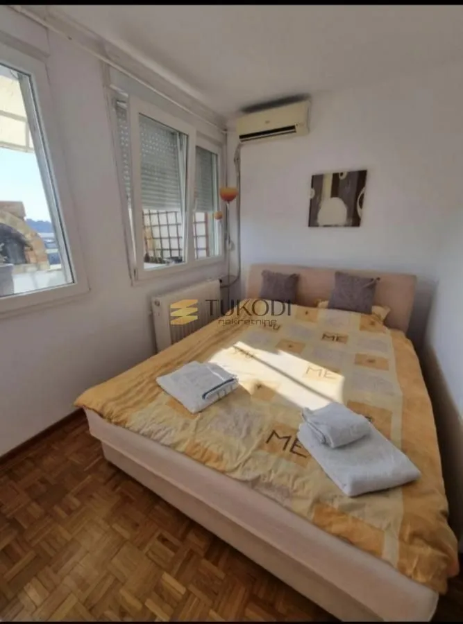 Furnished bedroom with a double bed, parquet flooring, and windows.