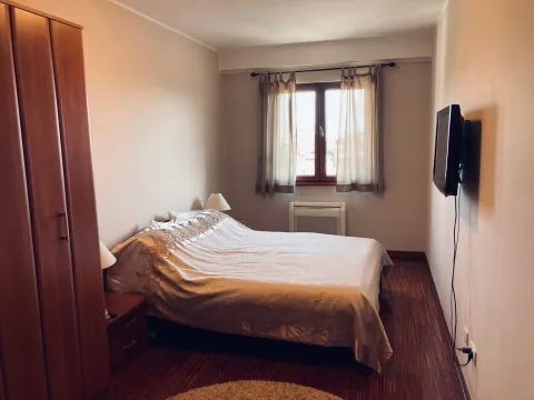 Uređena spavaća soba sa bračnim krevetom, ormarom i televizorom na zidu. - image 3