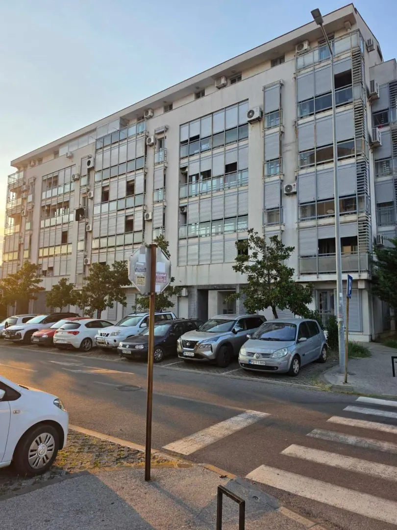Pogled na spoljašnjost stambene zgrade i parking ispred ulaza.