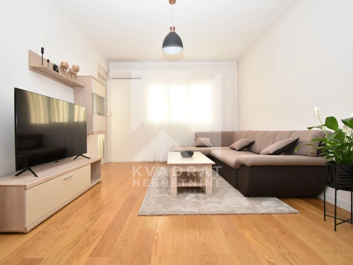 Living room furnished with a sectional sofa, TV, and wooden flooring.