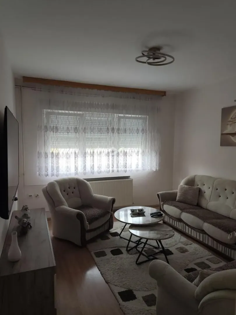 Dnevna soba sa garniturom, foteljom, stočićima i televizorom.