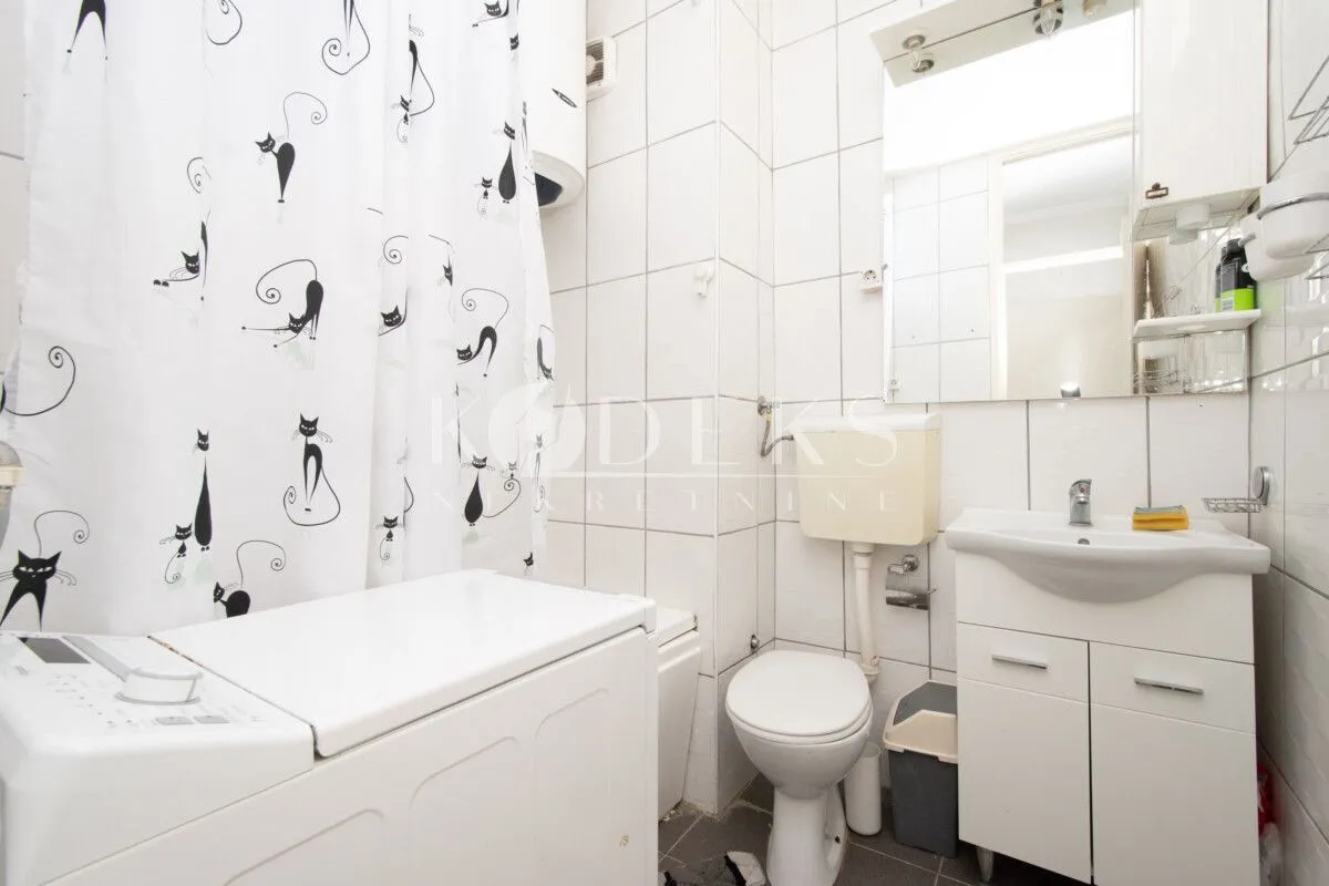 Small bathroom with white tiles, washbasin, toilet, and washing machine.