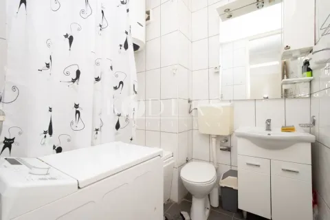 Small bathroom with white tiles, washbasin, toilet, and washing machine. - image 2