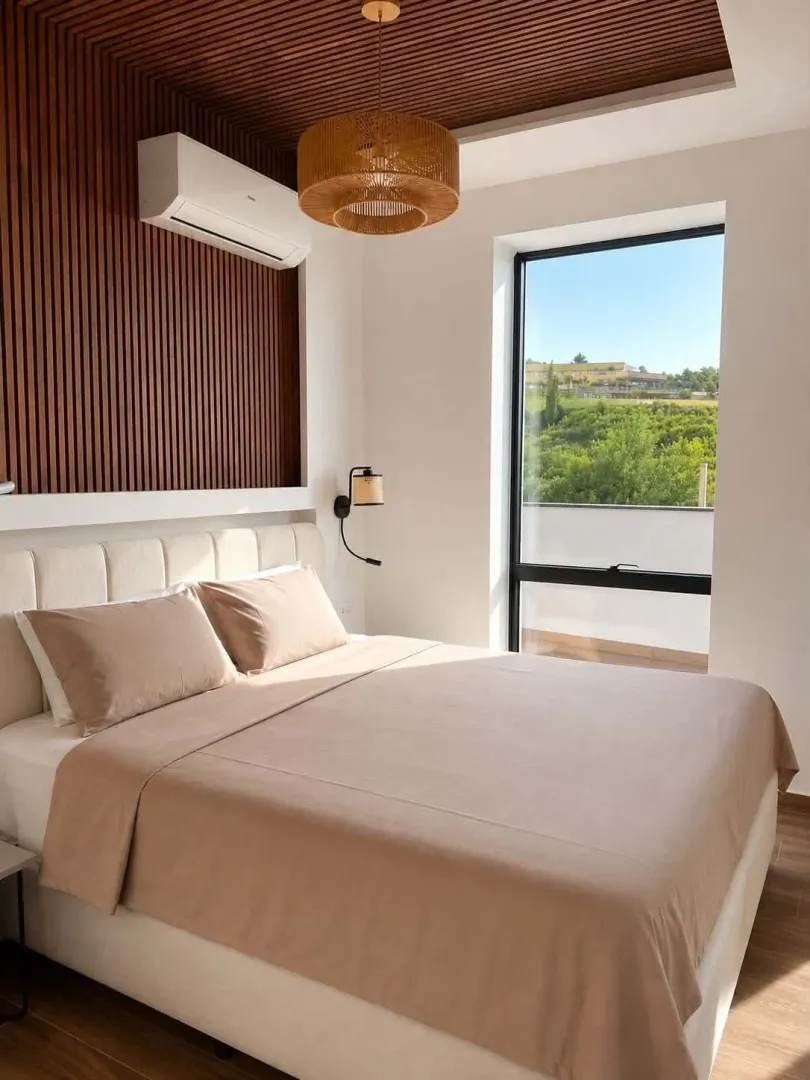 Modern bedroom with a double bed, wooden wall panels, and a view of nature.
