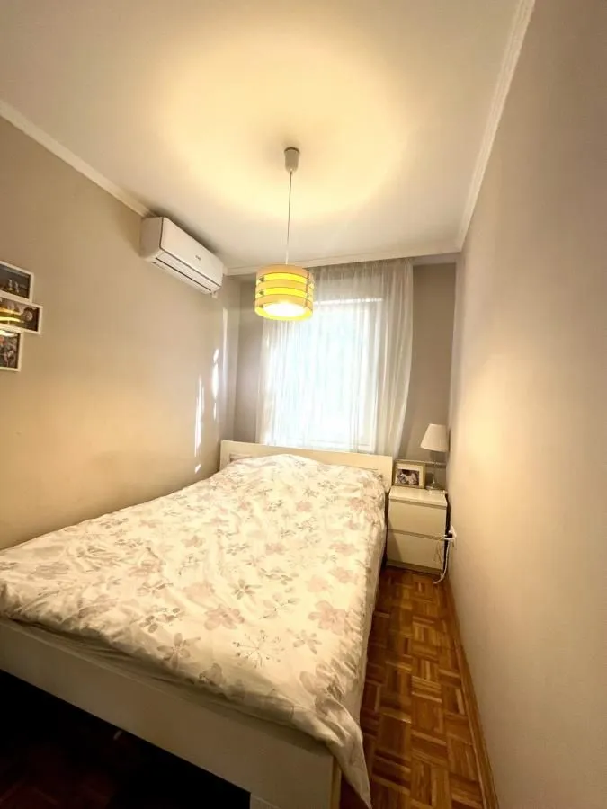 Manja spavaća soba sa bračnim krevetom, noćnim stočićem i klima uređajem.