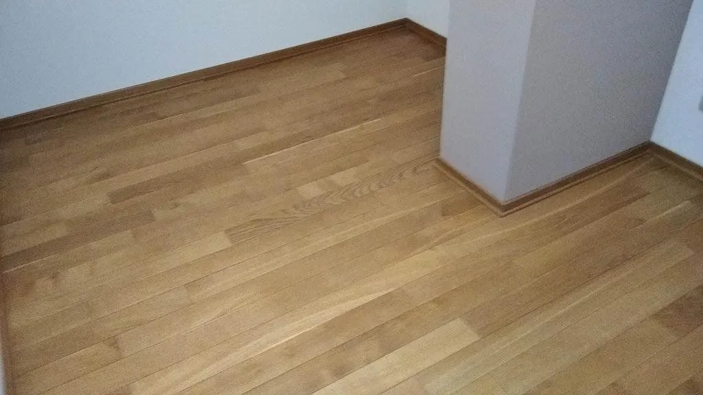 Pogled na drveni parket u praznoj prostoriji sa stubom.