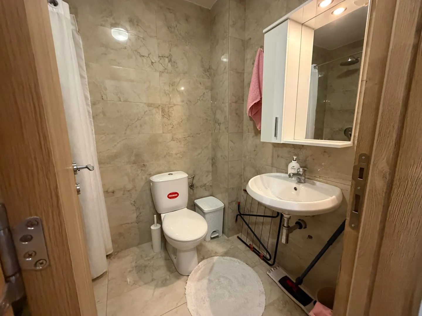 Manje kupatilo sa umivaonikom, WC šoljom i ogledalom sa ormarićem.